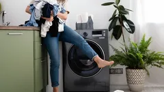 Žena načítá prádlo do pračky v moderní domácnosti s pokojovými rostlinami.