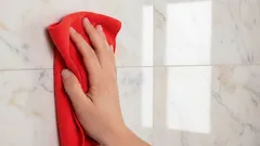 Čištění koupelnových dlaždic červeným hadříkem pro zářivý lesk a hygienu