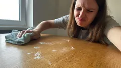 Žena s odporem utírá špinavý stůl hadrem v domácnosti u okna.
