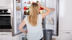 Žena přemýšlí před otevřenou lednicí v moderní kuchyni, hledá jídlo nebo inspiraci.