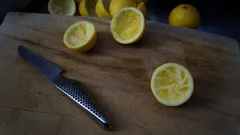 Nakrájené citrony na dřevěném prkénku vedle stříbrného nože