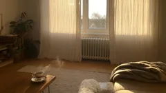 Slunný obývací pokoj s pohovkou, stolem a šálkem kávy, záclony před oknem.
