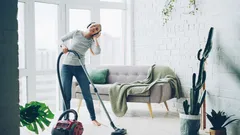 Žena vysává moderní obývací pokoj s vysavačem a sluchátky