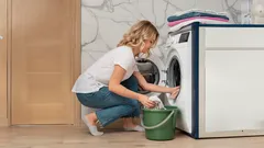 Žena vkládá prádlo do pračky v moderní domácnosti, příprava na praní.