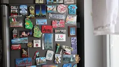 Lednice s barevnými magnety z cest kolem světa vedle okna s bílou záclonou