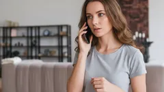 Žena v šedém tričku telefonuje v moderním obývacím pokoji