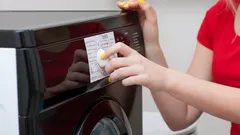 Žena nastavuje program pračky v červeném tričku, ovládání spotřebiče v domácnosti.