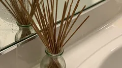 Aromatické tyčinky ve skleněné lahvi na umyvadle před zrcadlem v koupelně.