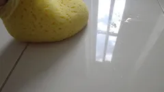 Žlutá pantofle na lesklé bílé dlažbě s odrazem okna na podlaze.