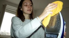 Žena čistí žehličku žlutým hadříkem v domácím prostředí