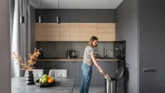 Žena v moderní kuchyni vyhazuje odpadky do koše, stylový interiér s ovocem na stole.